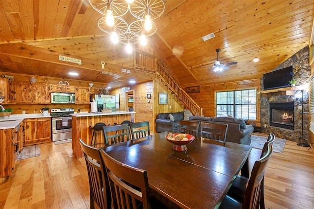 dining area featuring wooden ceiling, light wood-style floors, a fireplace, vaulted ceiling, and stairs