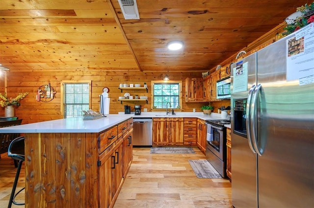 kitchen featuring appliances with stainless steel finishes, wood ceiling, a kitchen bar, light wood-type flooring, and brown cabinets