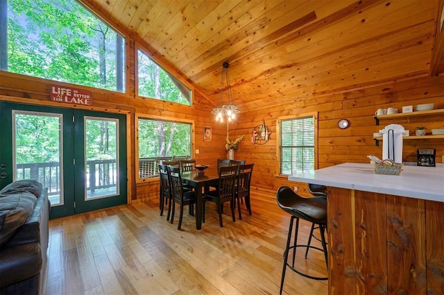 dining room with light wood-style floors, wood walls, high vaulted ceiling, wooden ceiling, and french doors