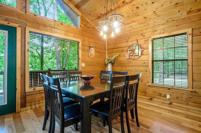 dining area featuring lofted ceiling, hardwood / wood-style floors, wood walls, plenty of natural light, and a chandelier