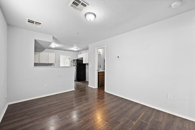 unfurnished living room featuring visible vents, dark wood-style flooring, and baseboards