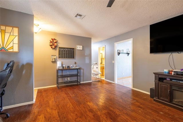 living area with baseboards, visible vents, wood finished floors, and a textured ceiling