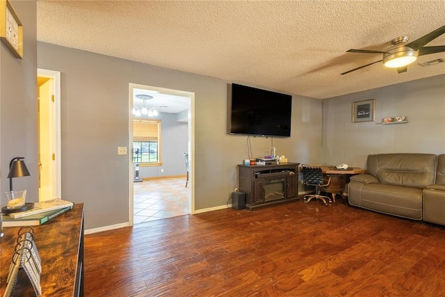 living room with wood finished floors, ceiling fan with notable chandelier, baseboards, visible vents, and a textured ceiling