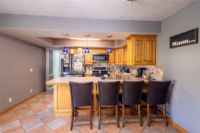 kitchen with a sink, stainless steel appliances, tasteful backsplash, a peninsula, and baseboards