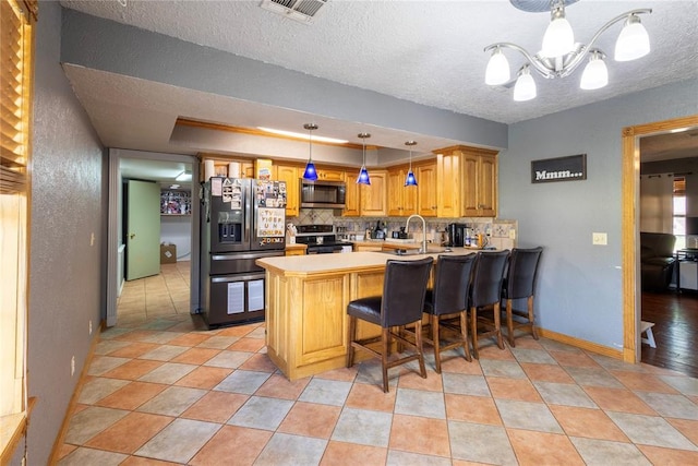 kitchen featuring tasteful backsplash, visible vents, stainless steel appliances, an inviting chandelier, and a peninsula
