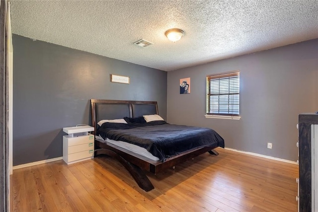 bedroom featuring a textured ceiling, visible vents, hardwood / wood-style floors, and baseboards