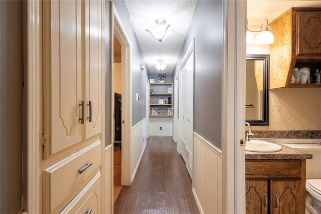 corridor featuring dark wood-style flooring, a textured ceiling, and a sink