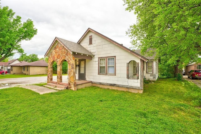 bungalow-style home featuring a front yard, stone siding, and a shingled roof