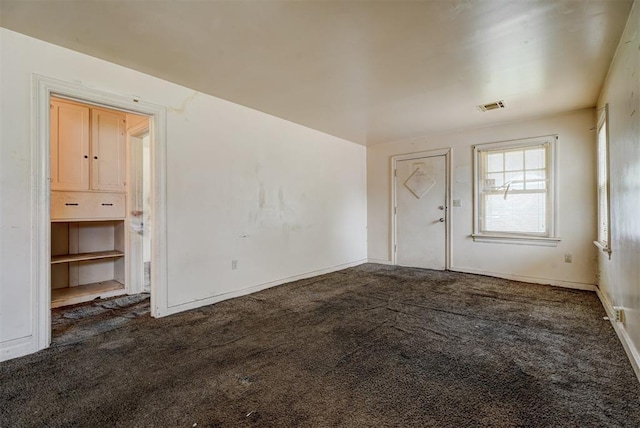 spare room featuring visible vents, dark carpet, and baseboards