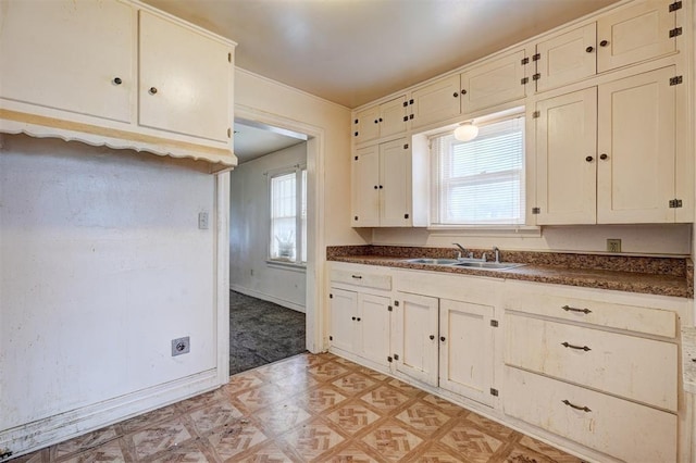 kitchen with light floors, dark countertops, baseboards, and a sink