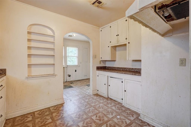 kitchen featuring arched walkways, light floors, dark countertops, baseboards, and visible vents