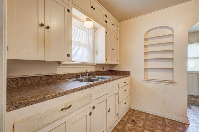 kitchen featuring baseboards, light floors, dark countertops, and a sink