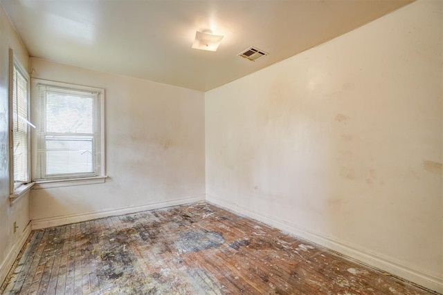 empty room featuring hardwood / wood-style floors, visible vents, and baseboards