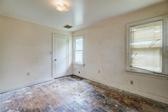 spare room with wood-type flooring, visible vents, and baseboards
