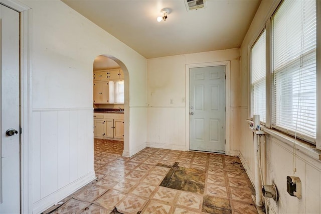 entrance foyer with light floors, visible vents, a wainscoted wall, and arched walkways
