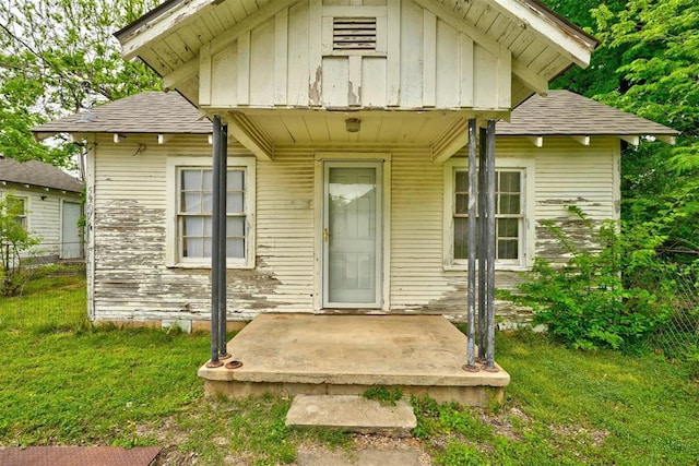doorway to property with fence, board and batten siding, a yard, and roof with shingles