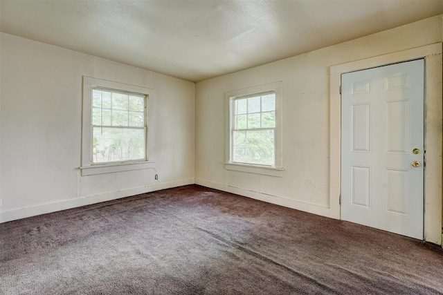 spare room featuring dark colored carpet and baseboards