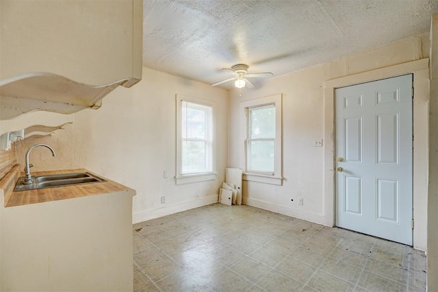 unfurnished dining area featuring a textured ceiling, a sink, baseboards, light floors, and a ceiling fan