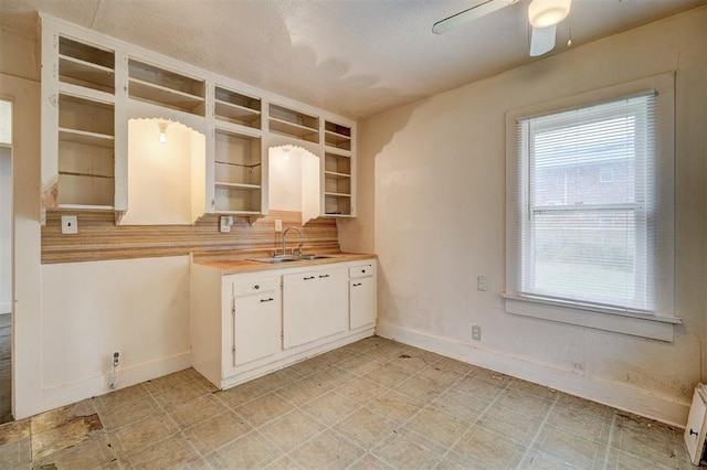 kitchen featuring open shelves, white cabinets, a sink, light countertops, and baseboards