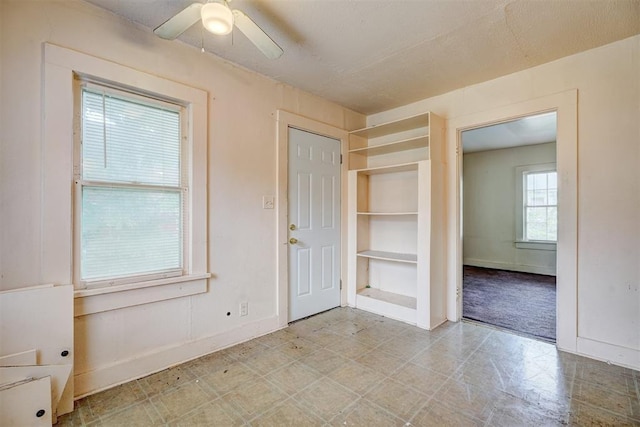 empty room with baseboards, built in shelves, and ceiling fan