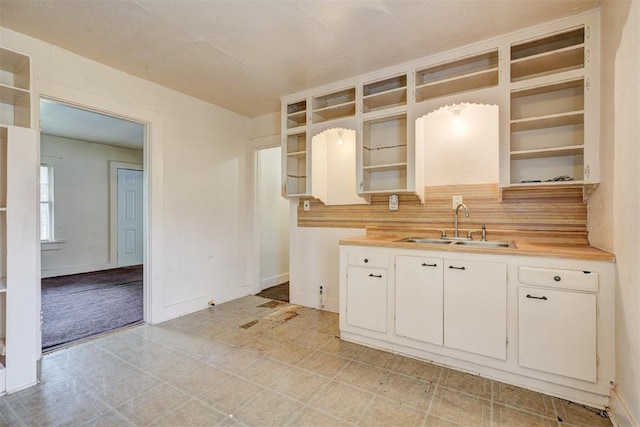 kitchen with light countertops, open shelves, backsplash, and a sink