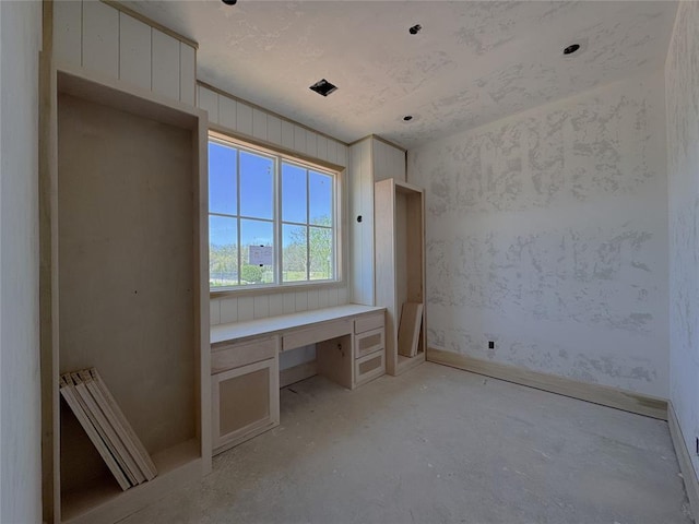 unfurnished room with built in study area and unfinished concrete floors