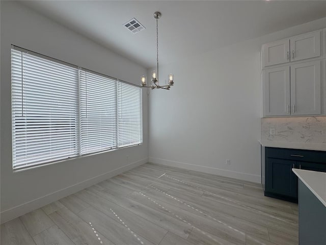 unfurnished dining area with baseboards, visible vents, an inviting chandelier, and light wood-style flooring
