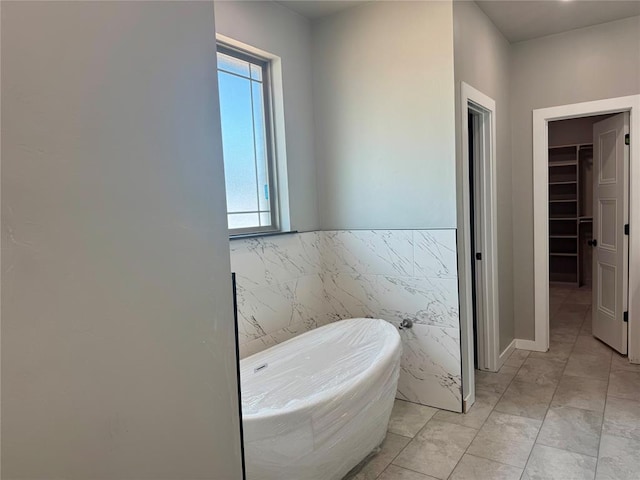 4129 Sambar St, Tuttle, OK 73089 - full bathroom featuring a freestanding bath, a spacious closet, tile walls, a wainscoted wall, and marble look tiles