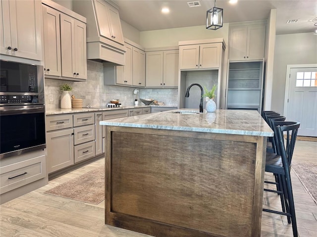 4129 Sambar St, Tuttle, OK 73089 - kitchen featuring black appliances, light wood-type flooring, light stone counters, backsplash, and a kitchen island with sink