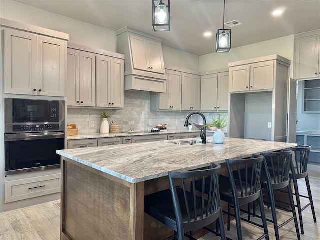 4129 Sambar St, Tuttle, OK 73089 - kitchen featuring black appliances, an island with sink, tasteful backsplash, light stone countertops, and light wood-style floors