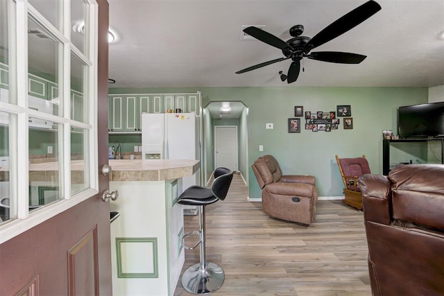 living area featuring arched walkways, ceiling fan, baseboards, and light wood-type flooring