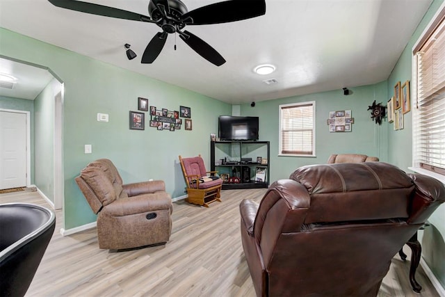 living room with ceiling fan, visible vents, light wood-style flooring, baseboards, and arched walkways