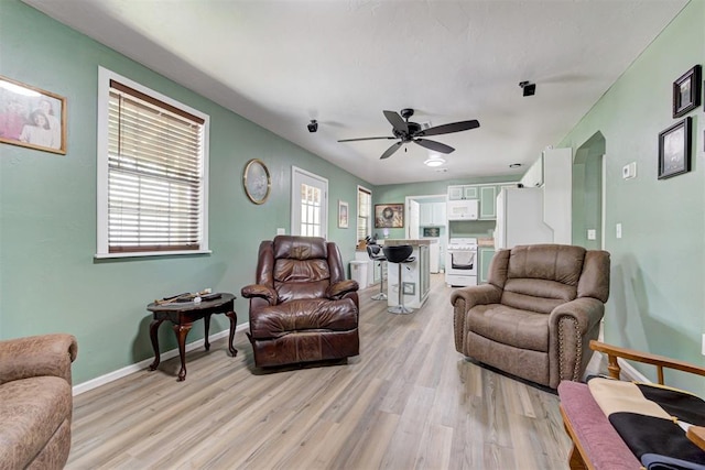 living area featuring a ceiling fan, baseboards, and light wood-type flooring
