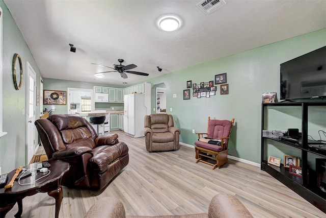 living room featuring arched walkways, light wood-style flooring, ceiling fan, baseboards, and visible vents