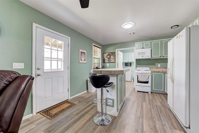 kitchen with white appliances, light wood-style flooring, a breakfast bar area, baseboards, and visible vents