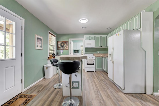 kitchen with white appliances, light wood-style flooring, a breakfast bar, light countertops, and a kitchen island