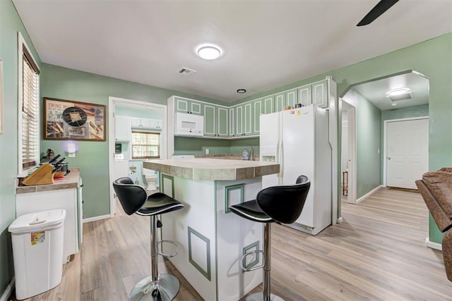 kitchen featuring a kitchen island, baseboards, a kitchen bar, light wood-type flooring, and white appliances