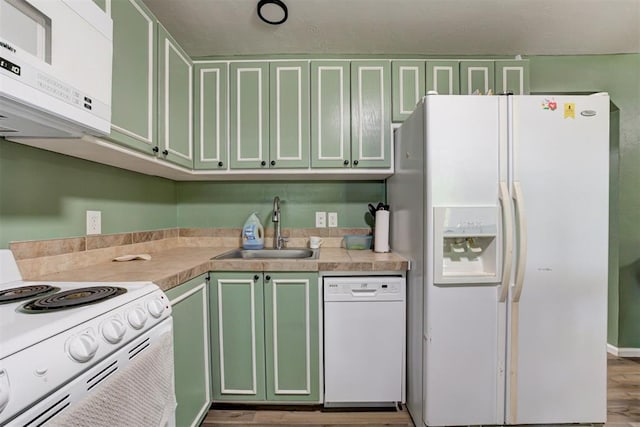 kitchen featuring wood finished floors, white appliances, light countertops, green cabinets, and a sink