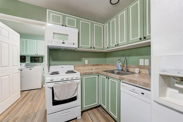 kitchen featuring green cabinetry, a sink, light wood-style floors, and white appliances
