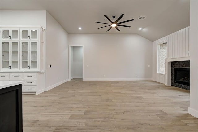 unfurnished living room featuring visible vents, light wood-type flooring, a ceiling fan, vaulted ceiling, and a premium fireplace