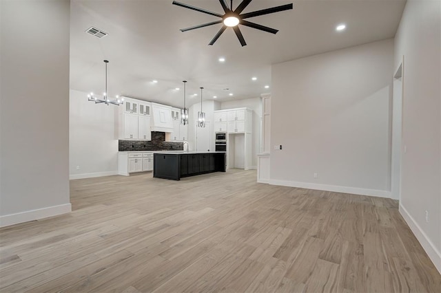 kitchen featuring visible vents, open floor plan, white cabinetry, ceiling fan with notable chandelier, and backsplash