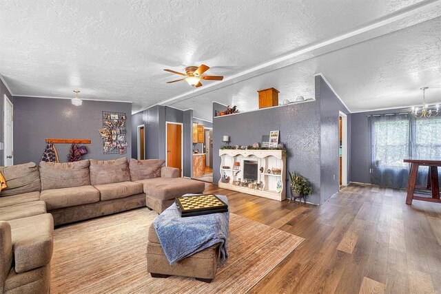 living area featuring ornamental molding, a textured wall, wood finished floors, a textured ceiling, and ceiling fan with notable chandelier