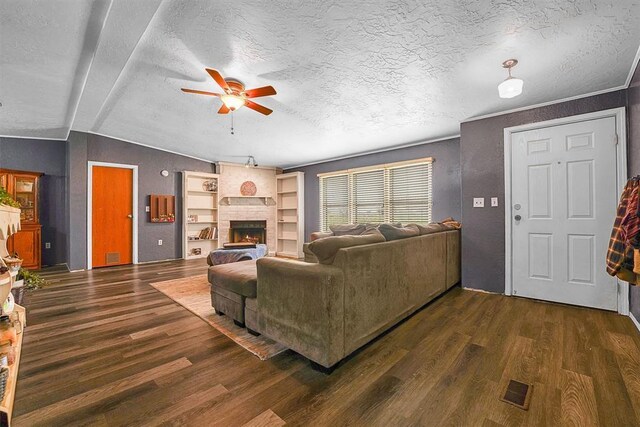 living area with ceiling fan, a brick fireplace, a textured ceiling, wood finished floors, and visible vents