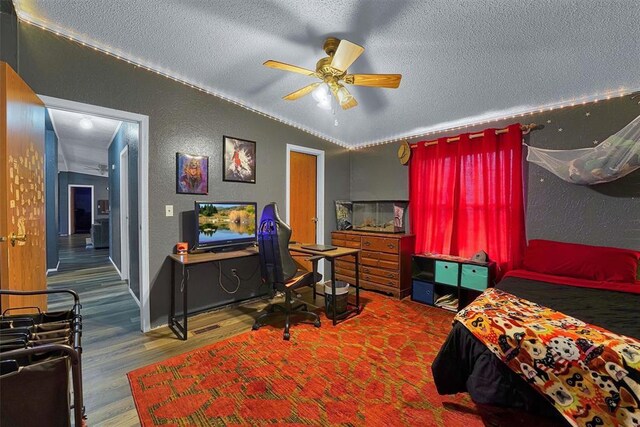 bedroom with a ceiling fan, a textured ceiling, wood finished floors, lofted ceiling, and a textured wall