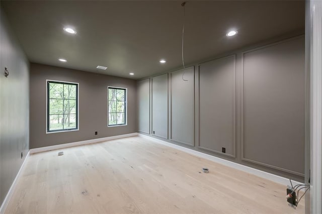 unfurnished room with a decorative wall, light wood-type flooring, and baseboards