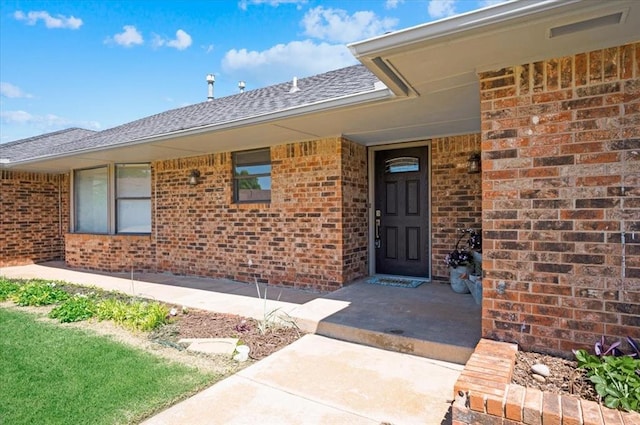 property entrance with a shingled roof and brick siding