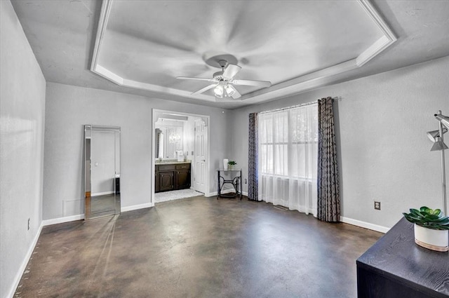 bedroom featuring baseboards, ensuite bathroom, a tray ceiling, a ceiling fan, and concrete floors