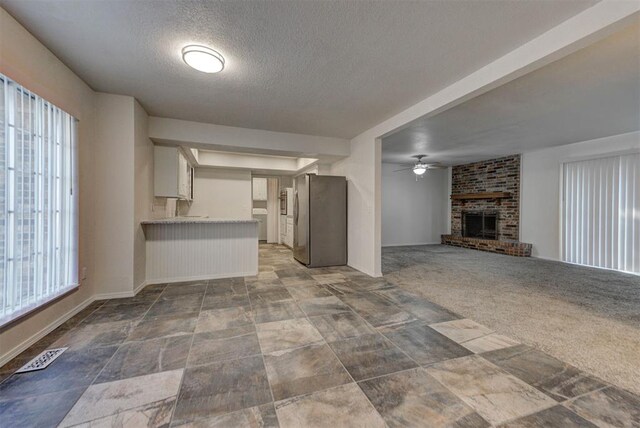 unfurnished living room featuring ceiling fan, stone finish flooring, a textured ceiling, visible vents, and a brick fireplace