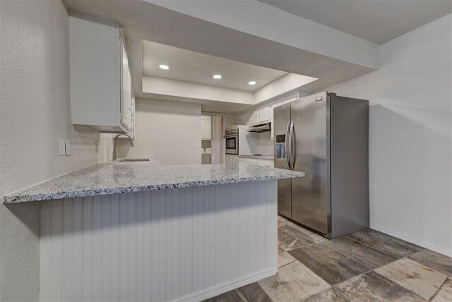kitchen with a peninsula, light stone countertops, white cabinetry, a sink, and appliances with stainless steel finishes
