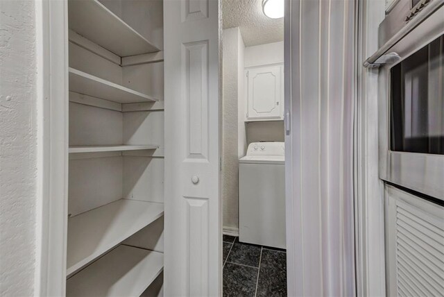 laundry area featuring dark tile patterned flooring, a textured ceiling, laundry area, and washer / clothes dryer
